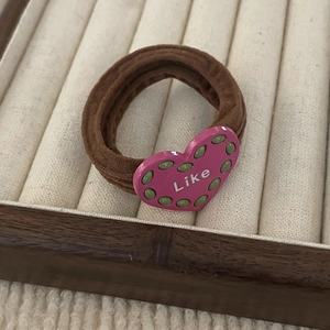 Detail of high-elastic coffee brown hair tie with a pink heart charm and Like lettering