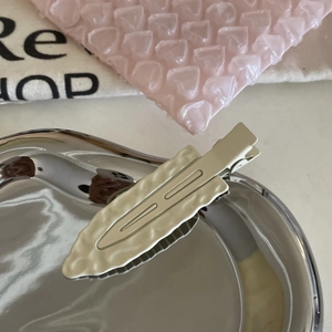 Macro detail of cream white wavy hair clip with silver metal duckbill base