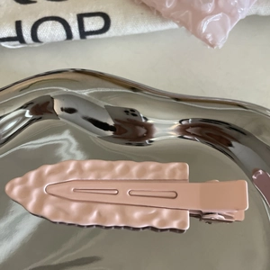 Close-up of matte pink duckbill hair clip with wavy texture and metal spring structure