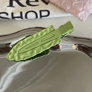 Detail of avocado green wavy hair clip on metallic tray with a matte frosted finish