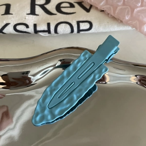 Close-up of matte blue leaf-shaped hair clip with hammer texture in silver tray