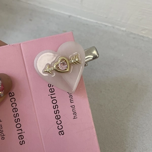 Détail macro d'une pince à cheveux cœur rose avec flèche dorée et strass brillant