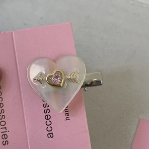 Détail de la pince à cheveux cœur rose avec flèche en strass sur carte décorative
