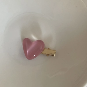 Detail of pink heart hair clip with cat-eye luster and golden metal duckbill base