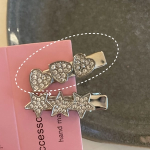 Détail de barrettes Y2K en argent avec étoiles et cœurs en strass sur carte rose
