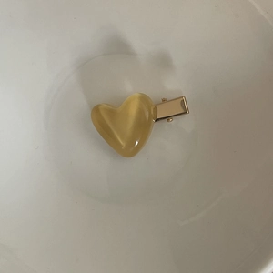 Detail view of a pale yellow resin heart hair clip with a golden metal duckbill clip