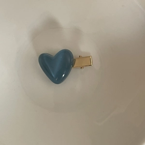 Minimalist blue heart resin hair clip with golden metal duckbill base on cream background