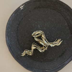 Pince à cheveux dorée en métal ondulé présentée sur une assiette en céramique grise