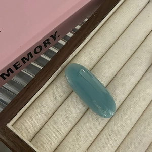 Detail of teal oval resin hair clip with elegant signature on premium velvet tray