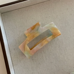Détail d'une pince à cheveux rectangulaire en acétate avec texture marbrée orange et verte