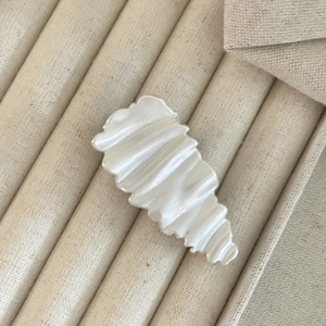 Elegant creamy white pleated hair clip with pearlescent finish on soft fabric background