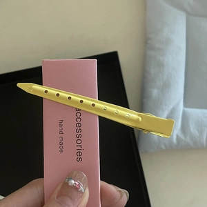 Gros plan sur une pince à cheveux en métal jaune mat avec trous sur carte rose