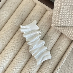 Chic milky white hair clip with rippled texture and pearlescent finish on beige fabric