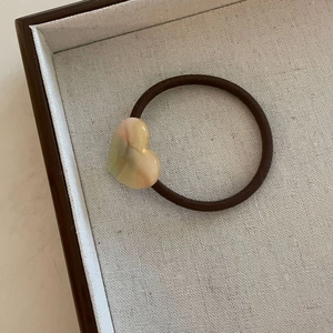 Détail d'un élastique à cheveux marron avec un charme en résine en forme de cœur marbré