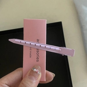 Détail d'une pince à cheveux en métal violet ajouré fixée sur un carton rose d'emballage