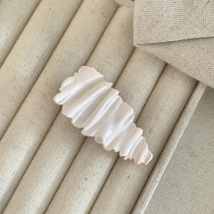 Macro shot of ripple textured hair clip in pearlescent creamy white on soft fabric