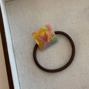 Détail du charme carré en acétate marbré multicolore sur élastique à cheveux marron