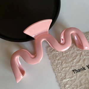 Vue rapprochée d'une pince à cheveux rose ondulée au fini brillant sur fond de carte décorative