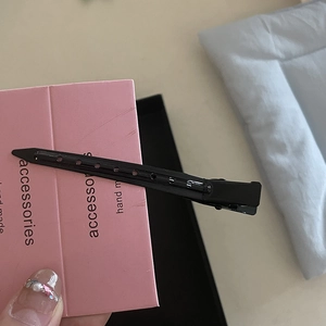 Gros plan d'une pince à cheveux en métal noir perforé sur sa carte d'emballage rose