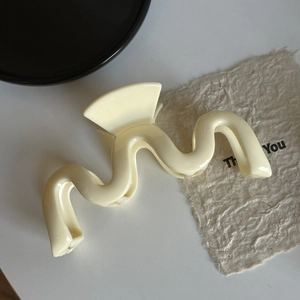 Détail d'une pince à cheveux ondulée blanc crème translucide sur un plateau décoré