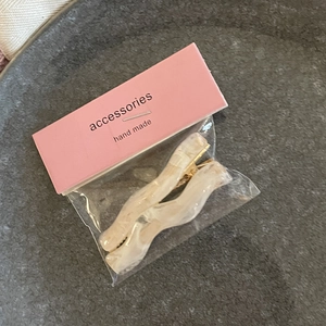 Detail of wavy cream marble hair clips with gold metal base in minimalist packaging