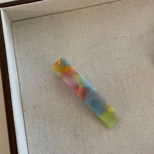 Vue détaillée d'une pince à cheveux rectangulaire en acétate marbré posée sur un plateau beige