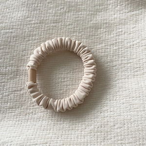 Minimalist beige pleated fabric hair scrunchie with silky texture on a textured background