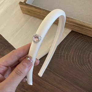 Pink satin padded headband with rhinestone heart detail shown on a wooden background
