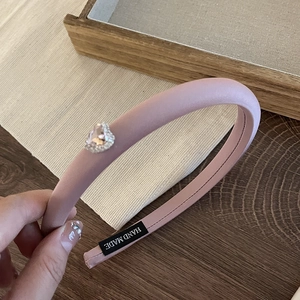 Detailed close-up of pink satin sponge headband with rhinestone heart and handmade label