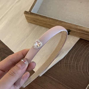 Detail of pink satin headband with sparkling rhinestone heart charm shown on wooden background