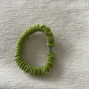 Detail view of grass green pleated elastic hair tie on a white fabric surface
