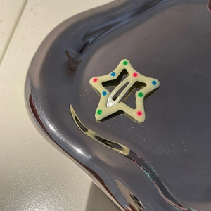 Cute cream star hair clip with colorful dots on a metallic display tray