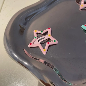 Close-up of a pink star-shaped metal hair clip with colorful dots on a silver tray