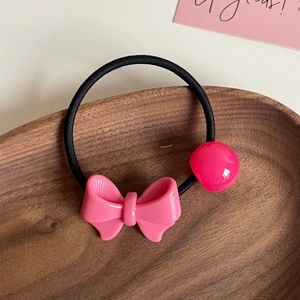 Dettaglio di elastico per capelli con fiocco rosa e perlina rossa in vassoio di legno
