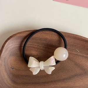 Dettaglio di un fiocco in acrilico crema e perla in resina su elastico nero per capelli