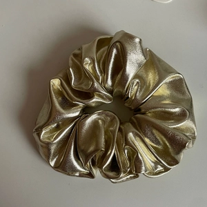 Metallic gold scrunchie hair tie with pleated elastic design on plain background