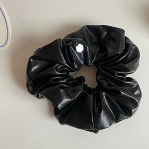 Detail of glossy black leather-like scrunchie with pleated texture and small white tag