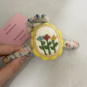 Detail of handmade wool-wrapped hair claw clip with colorful floral embroidery