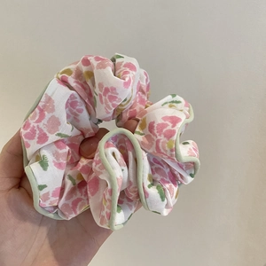 Détail d'un chouchou en tissu floral avec fleurs roses et bordure passepoilée verte