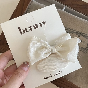Detailed macro view of a handmade cream ribbon hair clip on a display card