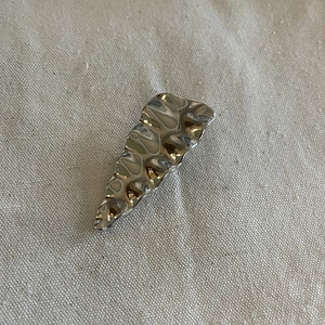 Silver wavy metal hair clip with hammered texture finish on a soft fabric background