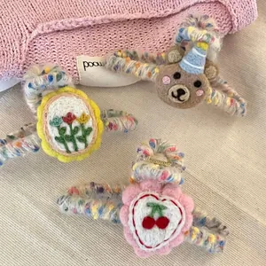 Three handmade strawberry and bear plush hair claw clips on a soft striped cloth