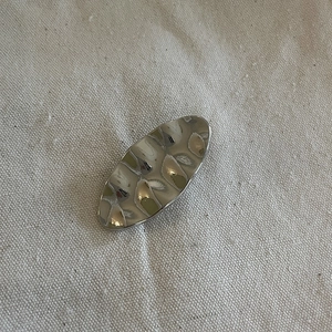 Silver wavy metal hair clip with irregular hammered texture on a neutral fabric background