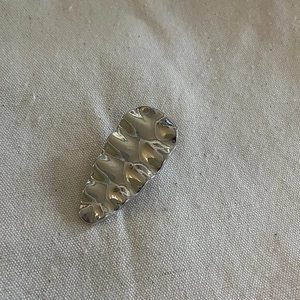 Silver minimalist wavy metal hair clip with lava texture on beige woven background