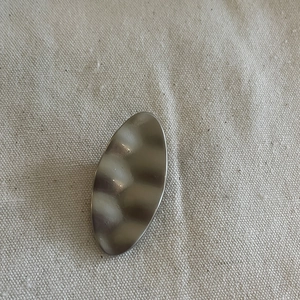Detailed view of silver wavy metal hair clip on minimalist cream fabric texture