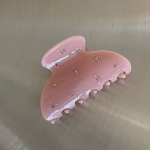 Detail of pink resin hair claw clip with floral rhinestone patterns on a silver surface