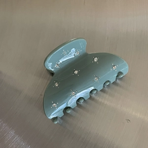 Detail view of a sage green semicircular hair claw clip with floral rhinestone clusters