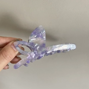 Gros plan détaillé de la pince à cheveux papillon en acétate nacré aux reflets violets