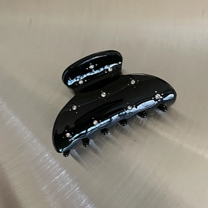 Detail of a black semicircular hair claw clip with embedded shiny silver rhinestones