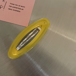 Translucent yellow oval candy hair clip with metal spring on a silver metallic background